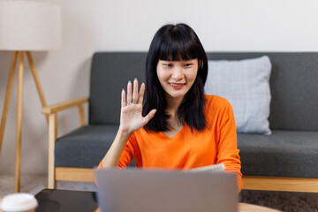 Fototapeta premium asian woman is sitting on a white couch in a modern home. Her is smiling and looking at her laptop freelance business online concept. 