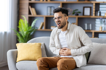 Man experiencing stomach pain sitting on sofa holding abdomen in discomfort