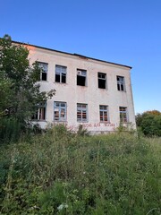 abandoned school brick building overgrown with grass and bushes with empty windows