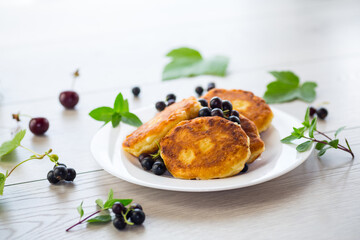 Fried curd cheese pancakes with black currants, on a wooden table