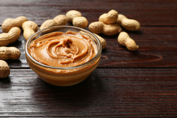 Tasty peanut butter in bowl and groundnuts on wooden table