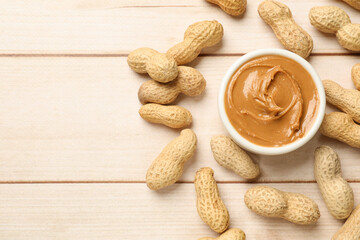 Tasty peanut butter in bowl and nuts on wooden table, flat lay. Space for text