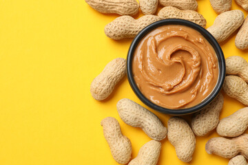 Tasty peanut butter in bowl and groundnuts on yellow table, flat lay. Space for text