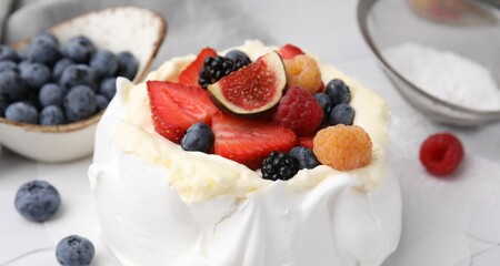 Pavlova cake (meringue dessert) with whipped cream, fresh berries and fig on table, closeup
