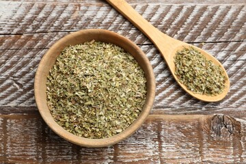 Dried oregano in bowl and spoon on wooden table, top view