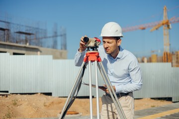 Civil Engineer Foreman in white protective helmet using level equipment. Surveyor s level at...