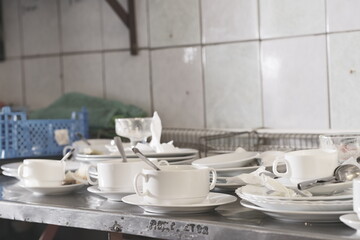 Dirty plates and glasses after a meal in the kitchen in the restaurant. Heap or pile of unclean glass and plates of breakfast or lunch table.