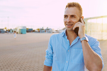Handsome young smiling man with brackets in a phone call outdoors at sunset. Businessman using...