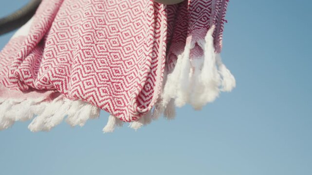 Red patterned towel blowing in the wind on a sunny day. Great for summer vacation or lifestyle projects. Perfect for travel vlogs showcasing beach destinations or relaxing lifestyle scenes.