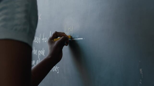 Cropped shot of unrecognizable African American male student writing on chalkboard while doing gap filling exercise during English lesson in classroom