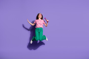 Full body photo of attractive young woman sing karaoke microphone jumping dressed stylish pink clothes isolated on violet color background