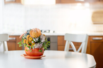 Thanksgiving day table setting decoration creative bouquet centerpieces with orange flowers in pumpkin as vase in modern home kitchen interior. Close up.