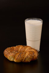 a pretzel with mixed seeds and a glass of kefir on a black background