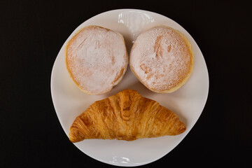 donuts filled with jam and a croissant on a white plate on a black background