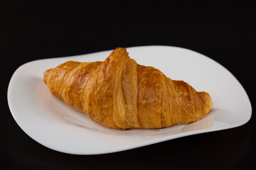 croissant with butter on a white plate with a black background
