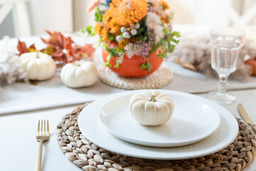 Thanksgiving day table setting with candles, fall decorations, centerpiece of dry flowers and pumpkin on white table in modern kitchen. Close up.