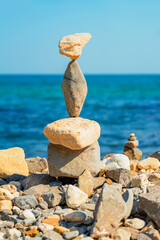 Balanced stack of stones on rocky beach, ocean and blue sky in background, harmony concept