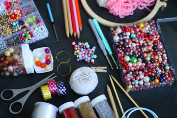 Colorful beads, coloring pencils, glitter, needles, string, hoop, tape and scissors on dark...