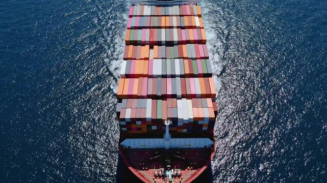 Aerial front view of a very large industrial container cargo carrier ship passing by with speed
