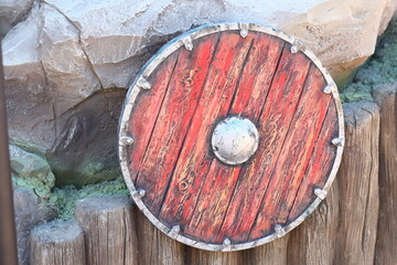 A wooden shield leans against a rugged rock wall in a natural setting