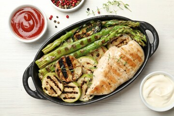 Delicious grilled vegetables and chicken breast in baking dish on white wooden table, flat lay