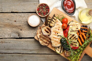 Delicious grilled vegetables and chicken breast served on wooden table, flat lay. Space for text