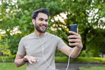 Smiling man enjoying engaging conversation on phone during fitness routine in park surrounded by greenery