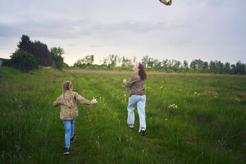 two little sisters and mother run and launch a kite in a field