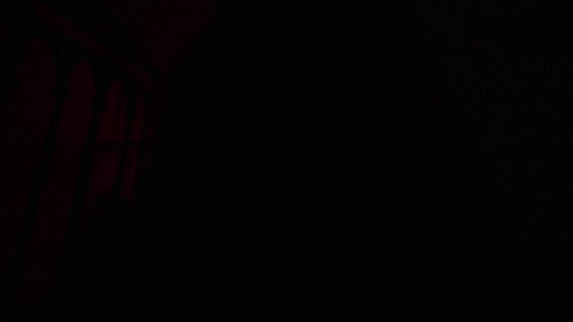 Creepy ghost woman in white dress and scary makeup alone on staircase in dark haunted house looks at camera in flashlight, close up. Halloween horror concept.