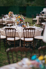 Outdoor Wedding Reception with Brown Chairs and Decorated Tables on a Green Lawn in a Scenic Nature Setting