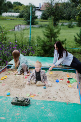 Mother with children playing in the sandbox on the playground. Happy childhood, having fun on weekends