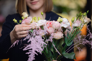 Happy young woman florist in suit collecting bouquet at workplace in flower shop