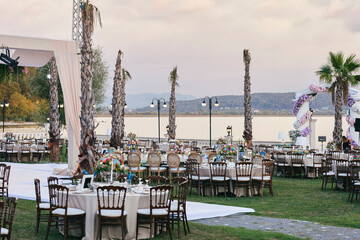 Elegant Outdoor Wedding Reception with Draped Canopy, Floral Centerpieces, and White Chairs...