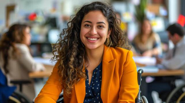 Smiling young woman in vibrant orange blazer in a wheelchair working in busy office environment