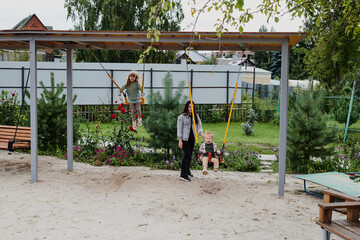 Mom swings her children on the playground. Happy childhood, fun weekends