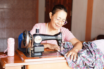 Happy senior Asian woman tailor is sewing cloth by vintage sewing machine at home. Concept, Senior ...