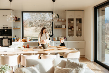 Mother arranging flowers in modern sunny kitchen preparing lunch with son