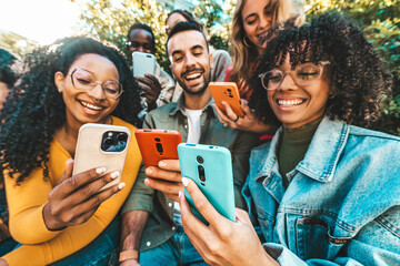 Obraz premium Group of young people using smart mobile phone outdoors - Happy friends with smartphone laughing together watching funny video on social media platform - Tech and modern life style concept