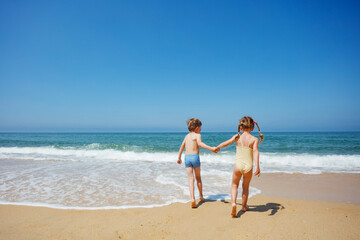 Naklejka premium Young friends laughing and running on the sea shore, hold hands