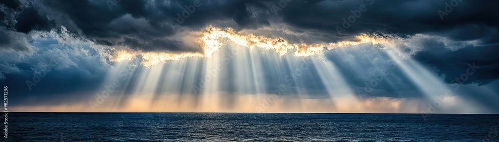 Aufkleber Dramatic landscape featuring rays of light piercing through dark clouds over the ocean, creating a serene and captivating atmosphere.