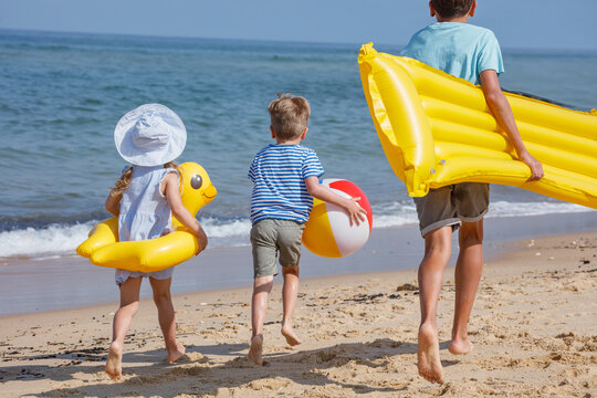 Children playing by the sea, carrying floaties and a beach ball