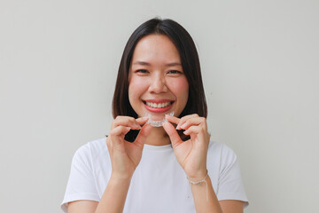 close up young asian woman smiling with hand holding dental aligner retainer (invisible) at dental...