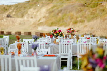 Outdoor Wedding Reception with White Chairs and Decorated Tables on a Green Lawn in a Scenic Nature Setting