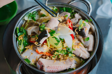 a hotpot filled with sour bamboo shoots and stingray pieces, garnished with herbs, showcasing a traditional Vietnamese dish. The broth is steaming, with vibrant colors and fresh ingredients.