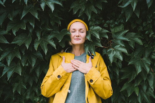 Portrait of relaxed and confident woman with eyes closed on background of green leaves wall. Thoughtful person in front of green hedge. Joy, zen and balance people. Stability through mental health