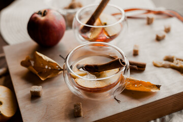 apple tea in glass cups with red apple slices and cinnamon stick, autumn tea, autumn drink, tea with brown cane sugar, autumn composition, fruit tea