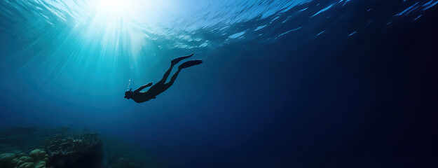 A diver swimming through the ocean as sunlight beams penetrate the surface above.