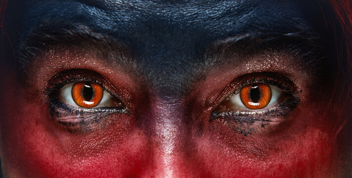 Close-up of a woman glowing demonic eyes with face partially painted in red and black. Demonic sinister character. Concept of Halloween, makeup, supernatural character. Flyer, banner.