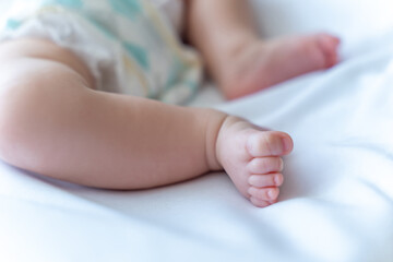 Unrecognizable infant child wearing diaper baby's feet on bed, copy space