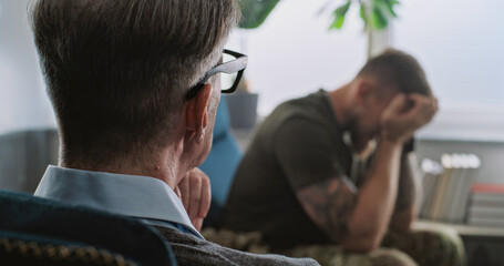 Back view of senior psychotherapist listening to soldier with PTSD. Depressed military man with post traumatic stress disorder cries during psychological therapy session with psychologist. Slow Motion